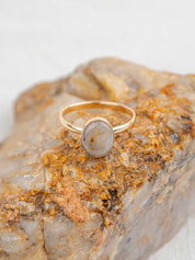 Gold ring with a polished oval stone sitting on the rock it was made from