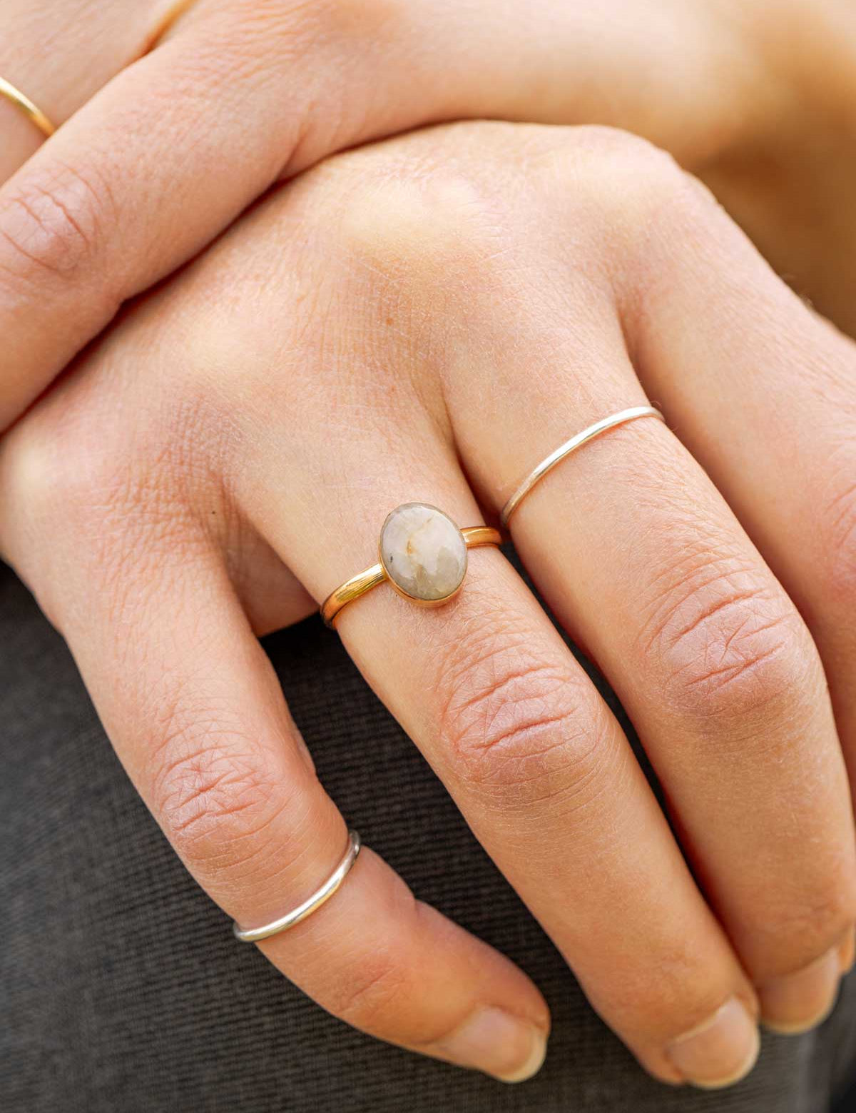 Close-up of a hand wearing a gold ring set with an oval stone