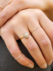 Close-up of a hand wearing a gold ring set with an oval stone