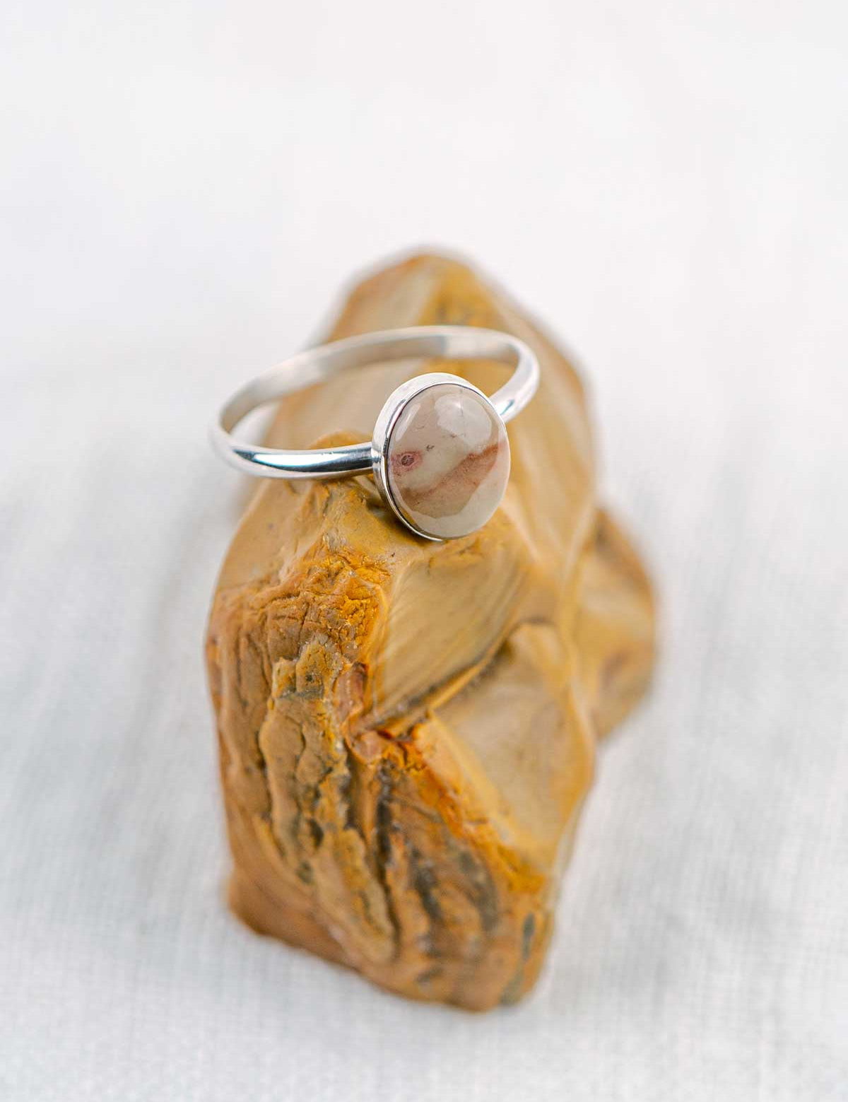 Silver ring with a polished oval stone sitting on the rock it came from
