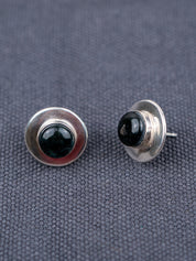 Pair of sterling silver stud earrings featuring round black jade stones, photographed on a textured gray fabric background, shown from front and side angles.