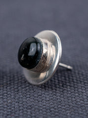 Sterling silver stud earring with a domed black jade stone, shown in close-up from a side angle on a textured gray fabric background.