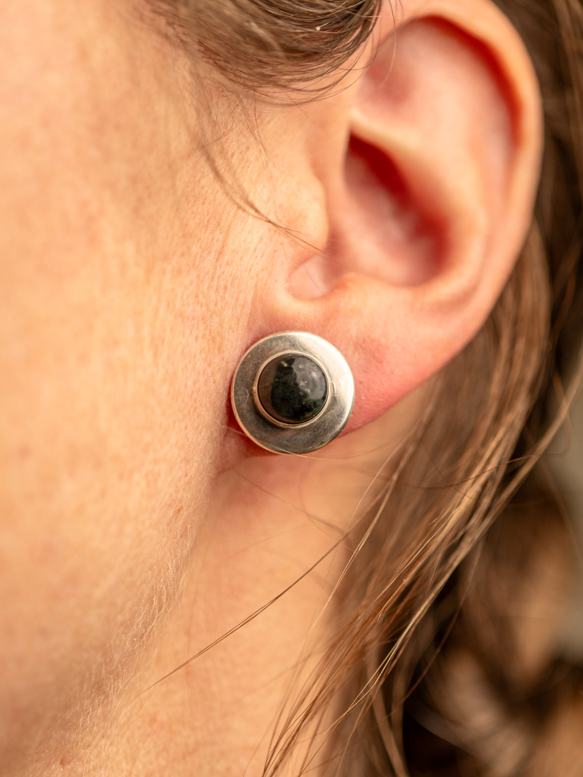 Sterling silver stud earring with a domed black jade stone, shown in close-up on a person's ear