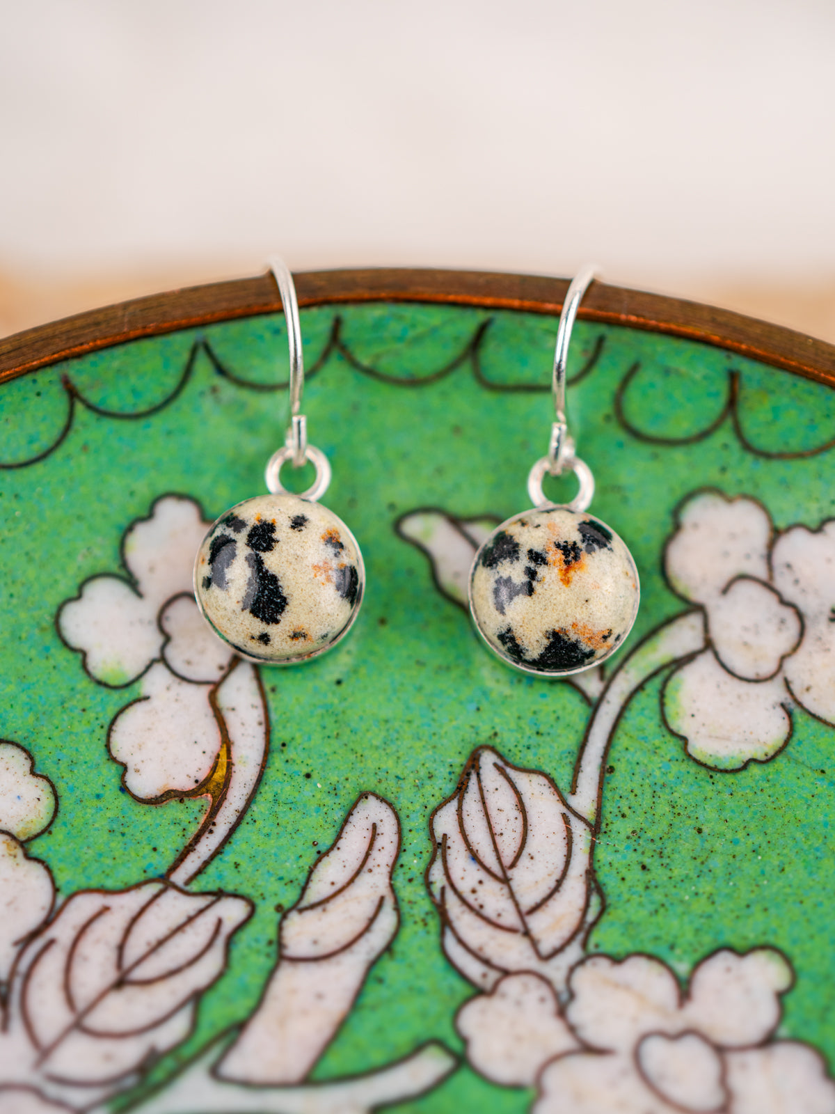 Round earrings with black and orange speckles on a floral green plate