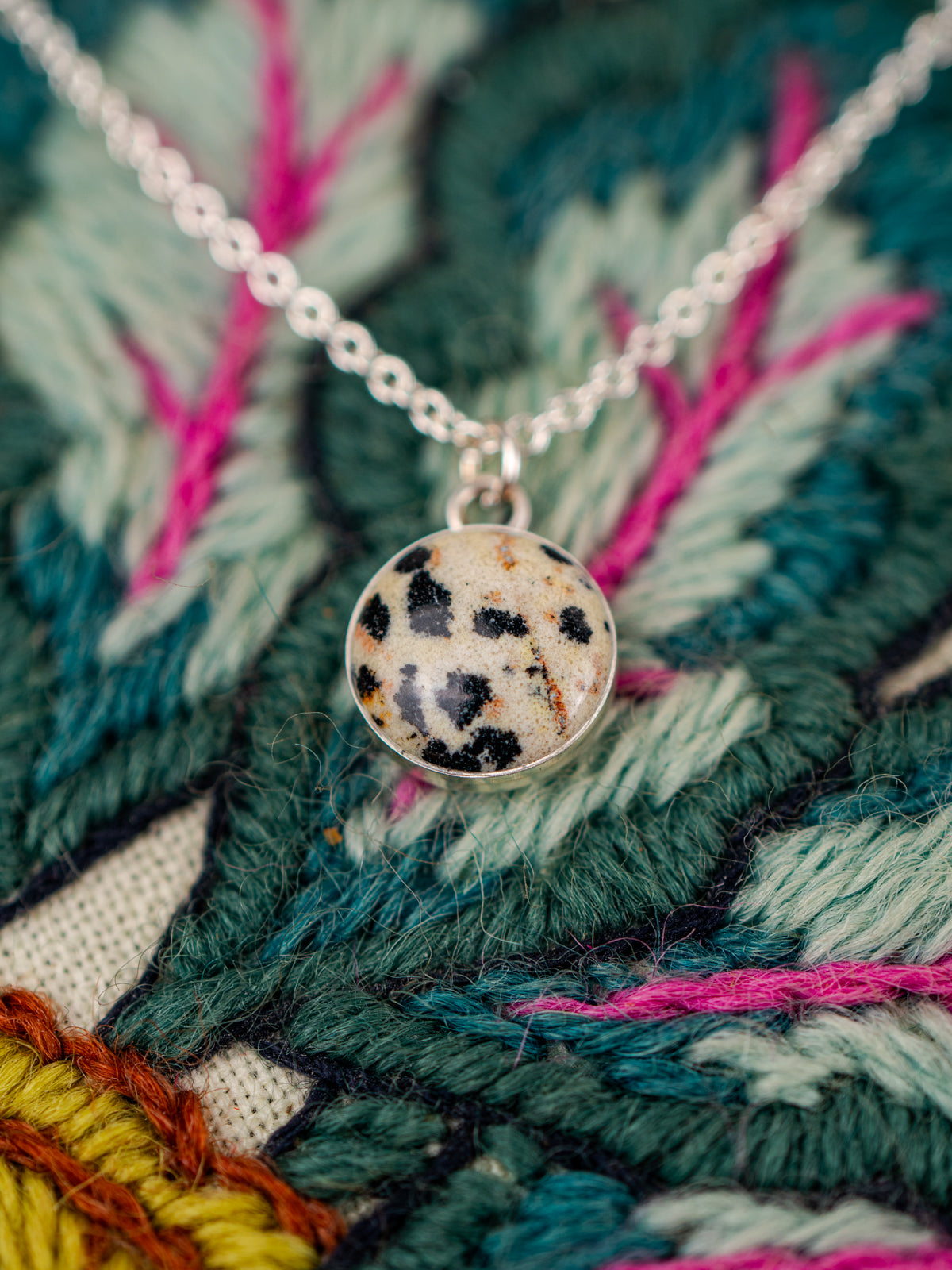 Necklace with a round pendant on a colorful embroidered fabric background
