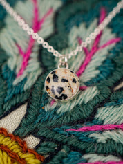 Necklace with a round pendant on a colorful embroidered fabric background