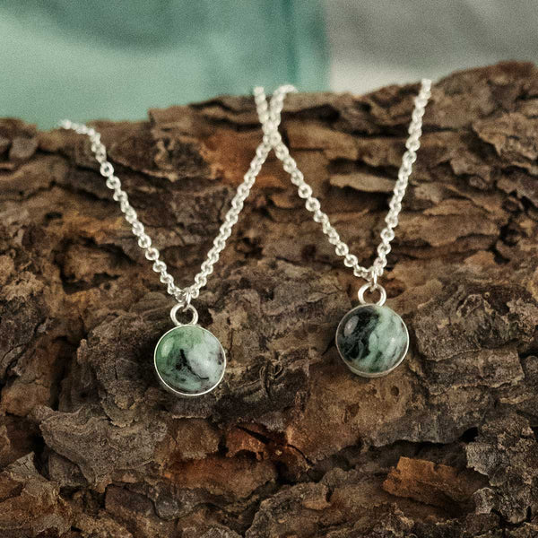 Two sterling silver pendant necklaces with small round green stones on a wooden surface