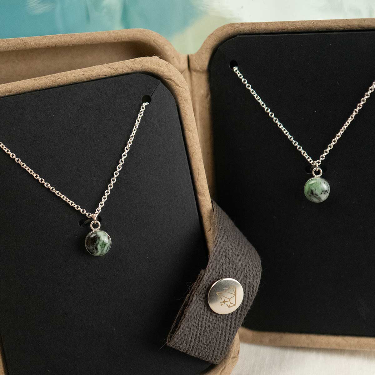 Two matching necklaces with a green stone pendant on a black display card inside a brown jewelry box.