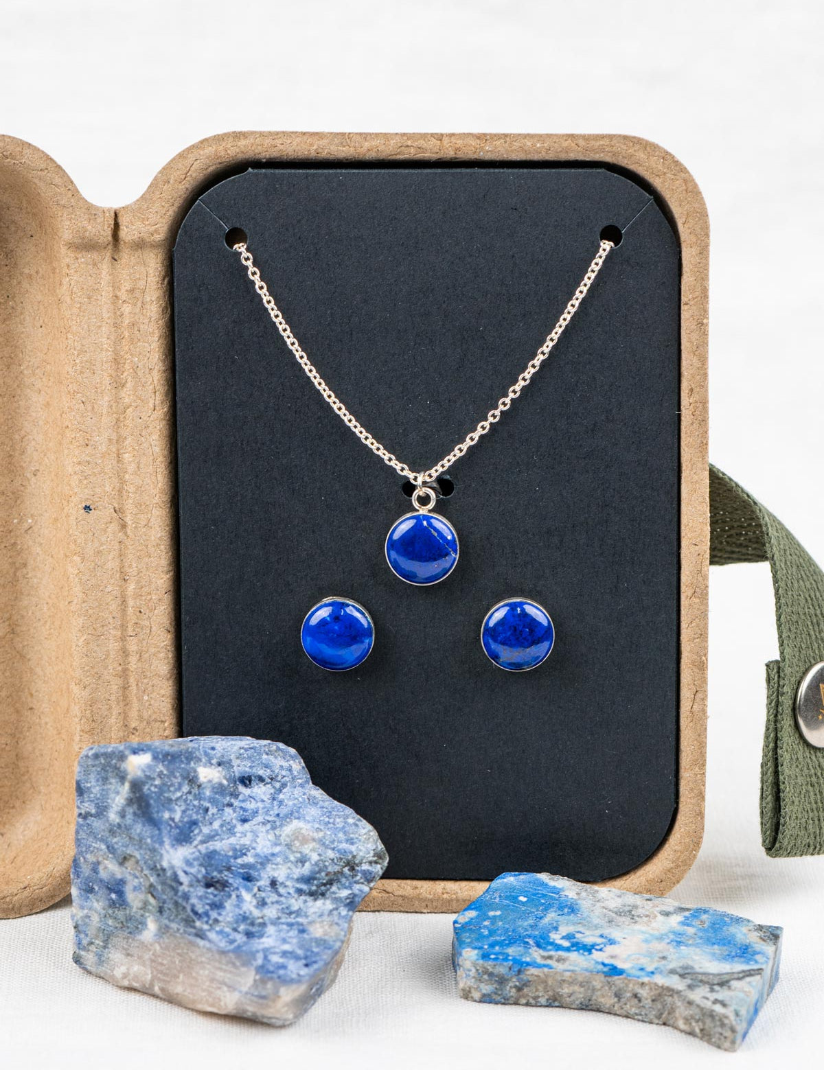 Necklace and earring jewelry set with blue stones in a kraft gift box, surrounded by the rocks they were made from