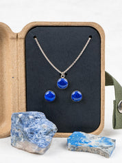 Necklace and earring jewelry set with blue stones in a kraft gift box, surrounded by the rocks they were made from