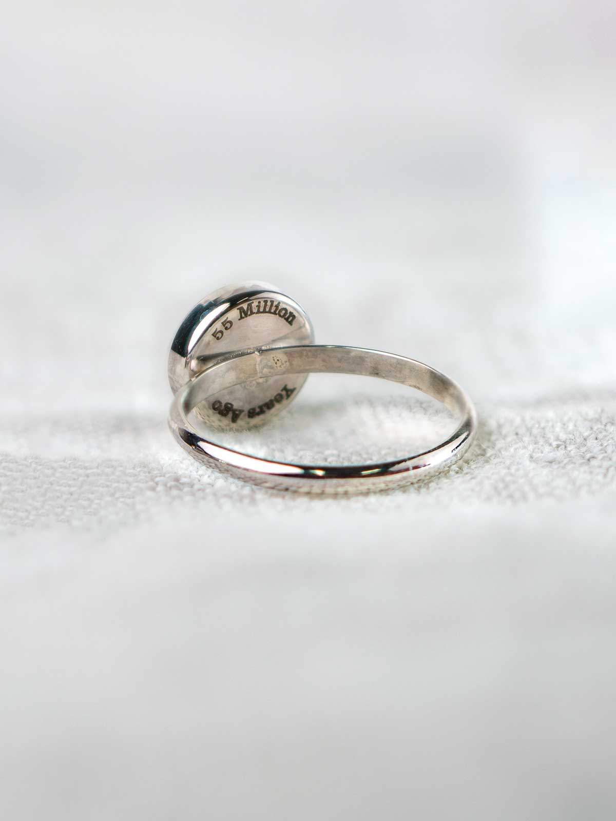 Silver ring with engraved text on the back of its round stone