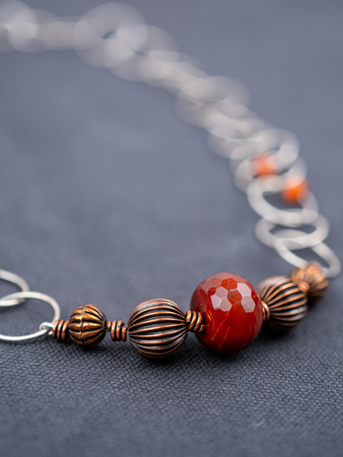 Close-up of the Faceted Fire Agate with textured beads, photographed on a gray background