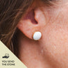 Close-up of an ear wearing a white stone stud earring set in 14k gold fill and engraved on the edge; text "you send the stone" in the corner