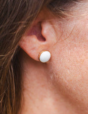Close-up of an ear wearing a white stone stud earring in a 14k gold fill setting that's engraved with text on the edge