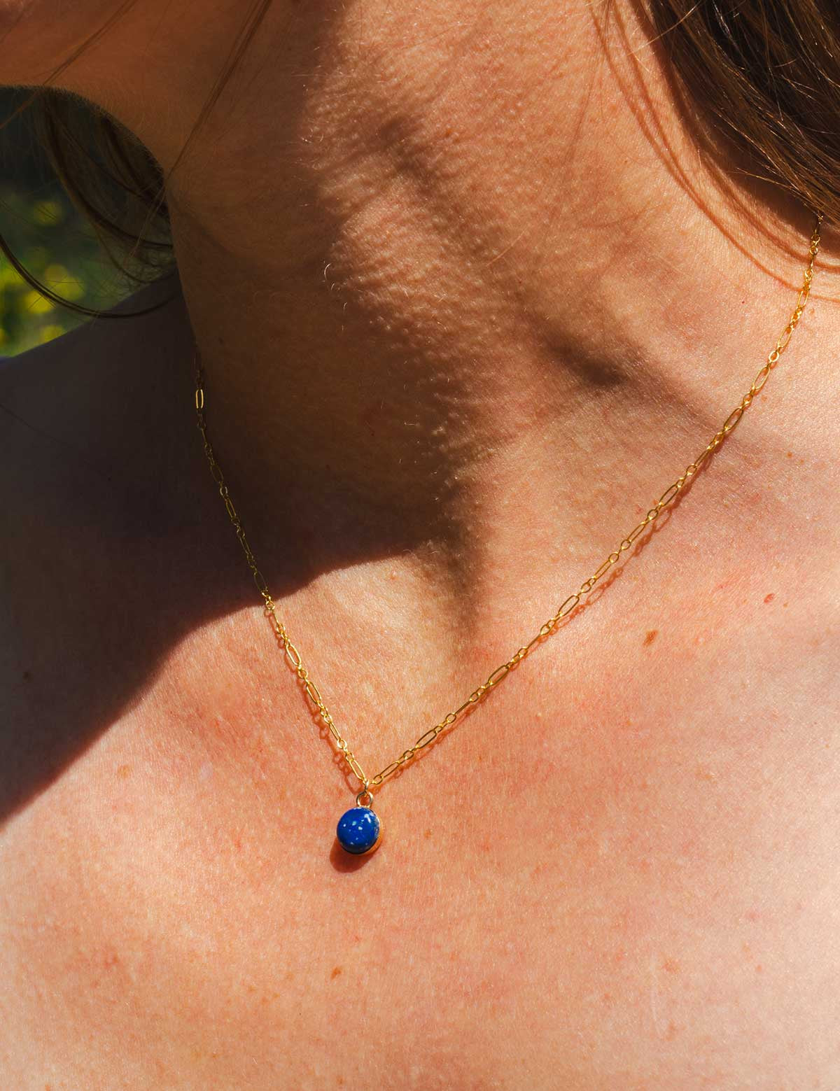 Gold necklace with a blue lapis lazuli pendant worn by a woman outdoors