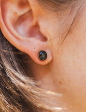 Close-up of an ear wearing a gold fill stud earring set with a natural black rock. The earring is engraved on the edge of the setting.