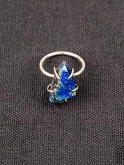 Silver ring with a deep blue lapis stone held securely by a prong setting, displayed on a dark fabric background.