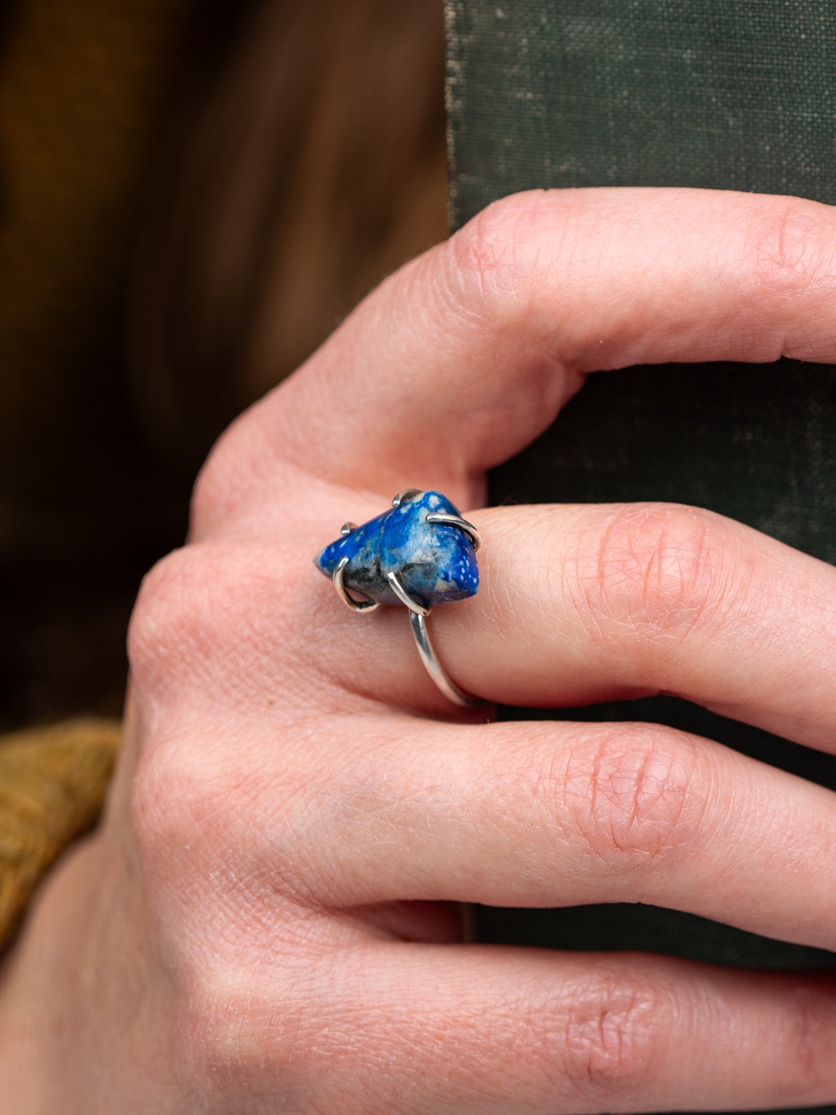 Silver ring with a deep blue lapis stone held securely by a prong setting, displayed on a hand holding a book.