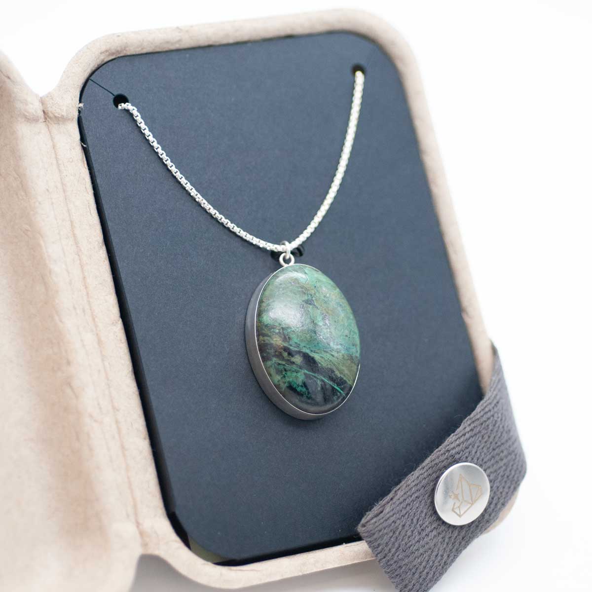 Natural green stone set as an oval pendant, packaged in a kraft gift box
