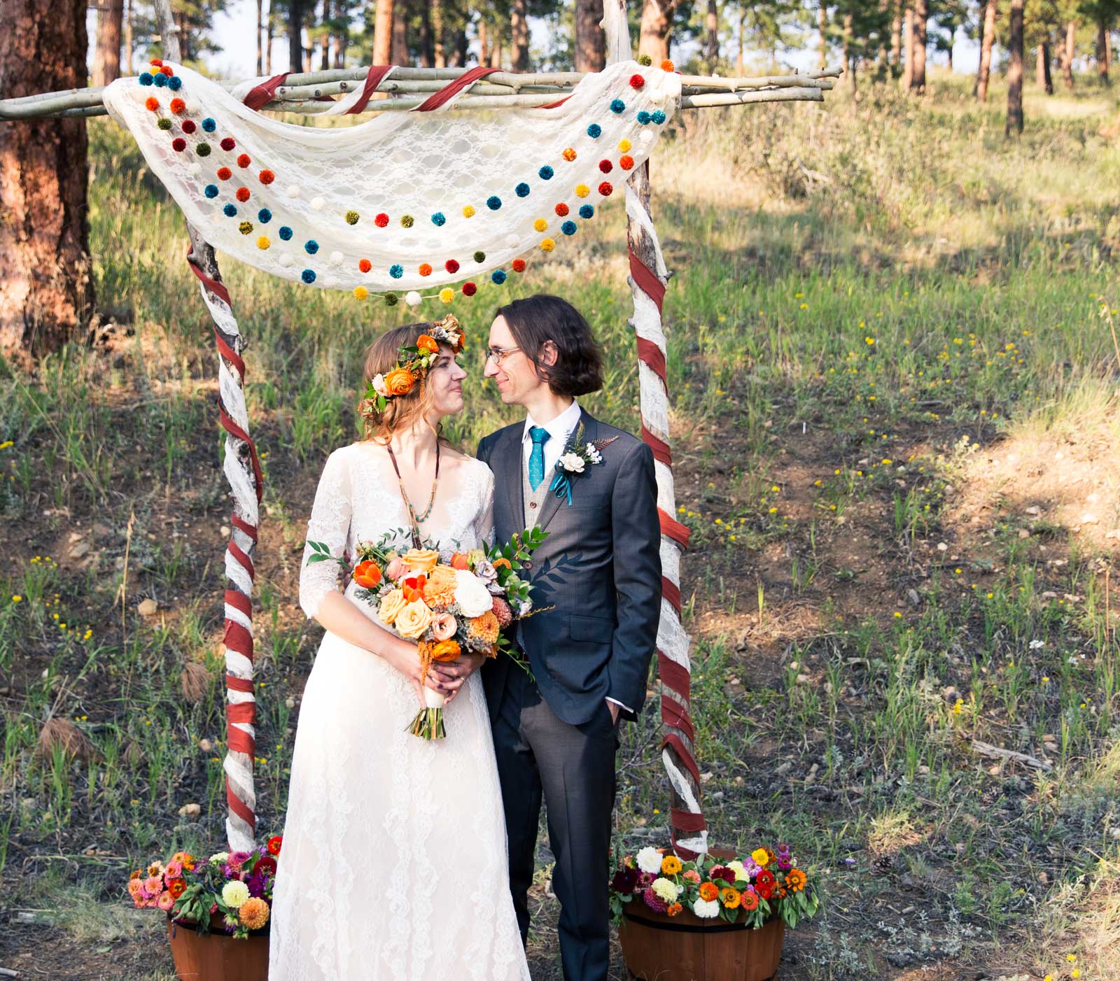 Leslie and her husband Sean standing under a colorful wedding arch in a forest setting
