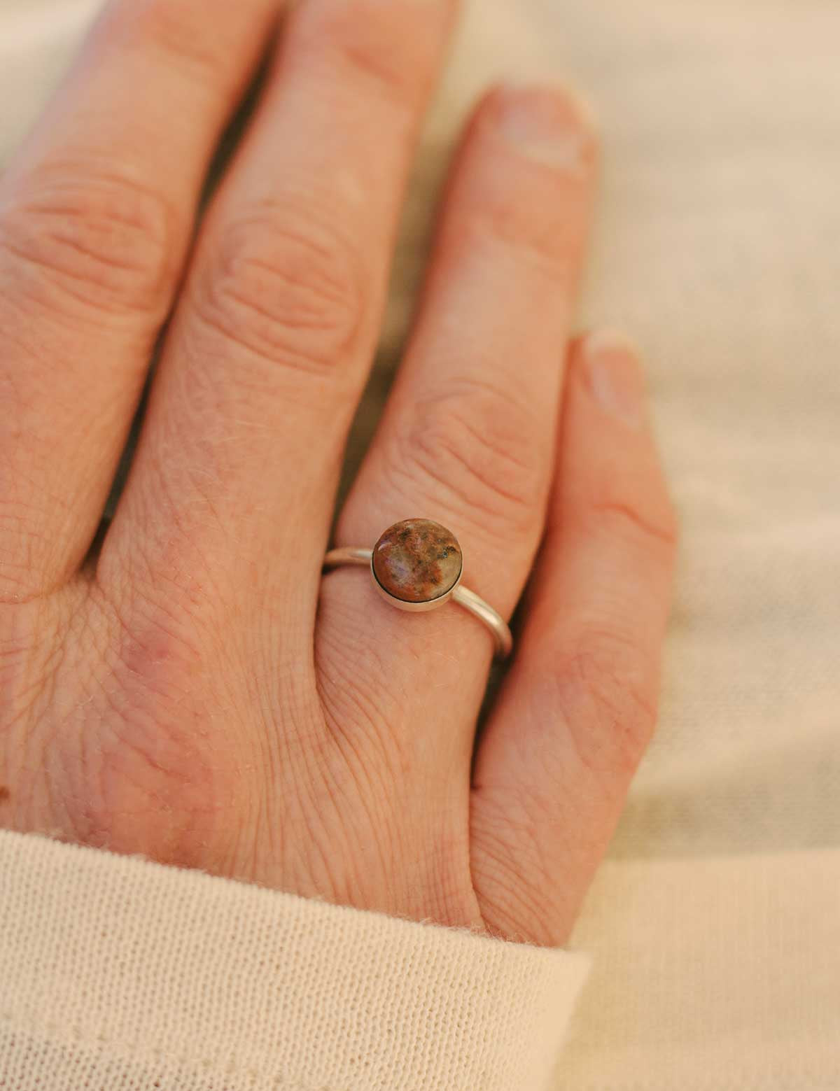 Hand wearing a sterling silver ring set with a natural brown stone