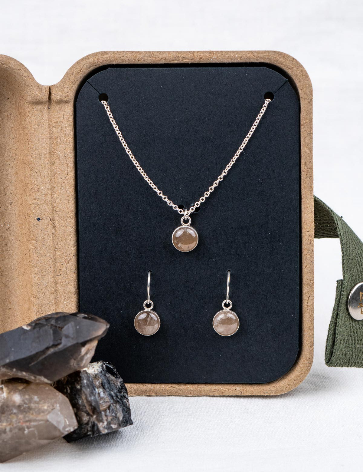 Custom jewelry set with necklace and earrings made from the same gray crystal, displayed in an open kraft jewelry box