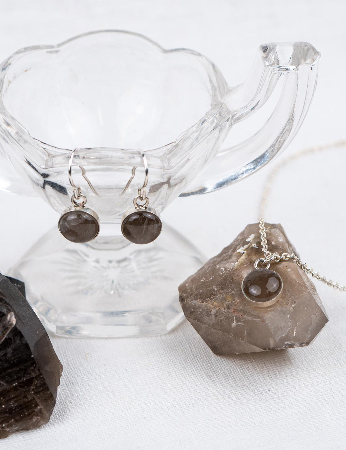 Custom matching jewelry set with dangle earrings and a pendant necklace made from gray crystal, displayed with the original rocks they were made from
