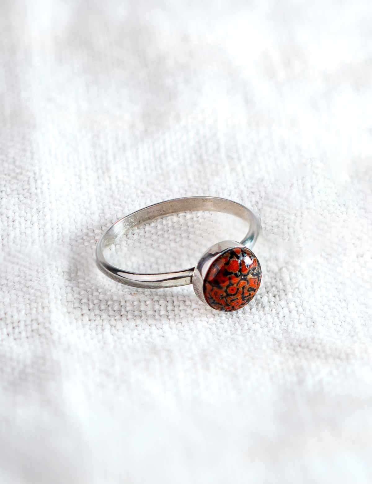 Sterling silver ring with a red and black speckled stone in a round setting