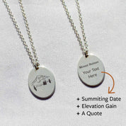 The front and back of a voyager charm necklace with a mountain design. Customize your own engraving for the back. Engrave your name, a summit date, elevation gain, or a quote.