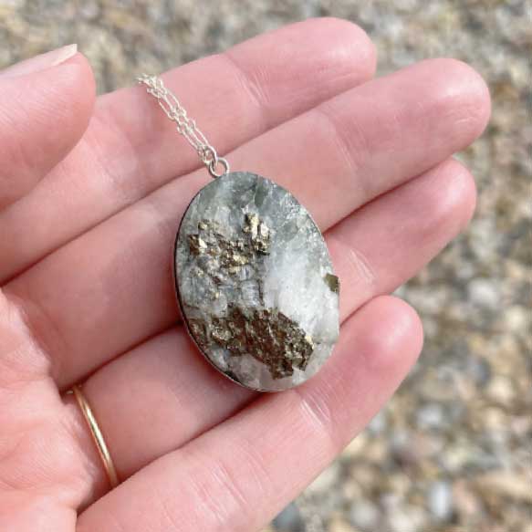 Hand holding a necklace with a pendant featuring a rough-surfaced natural stone with mica and quartz inclusions