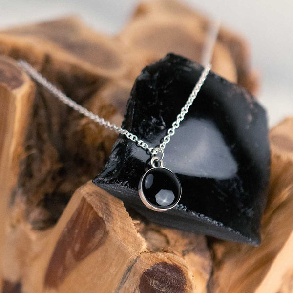 Black obsidian pendant necklace on a wooden surface with the rock it was made from