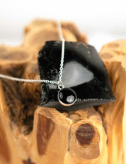 Black obsidian pendant necklace on a wooden surface with the rock it was made from