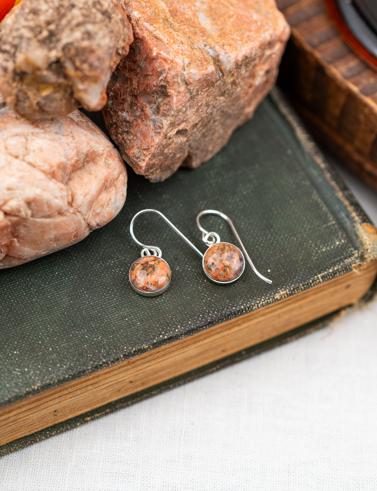 Silver earrings with round pink stones on a book with rocks in the background