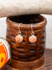 Pair of earrings with round pink stones in a wooden holder.