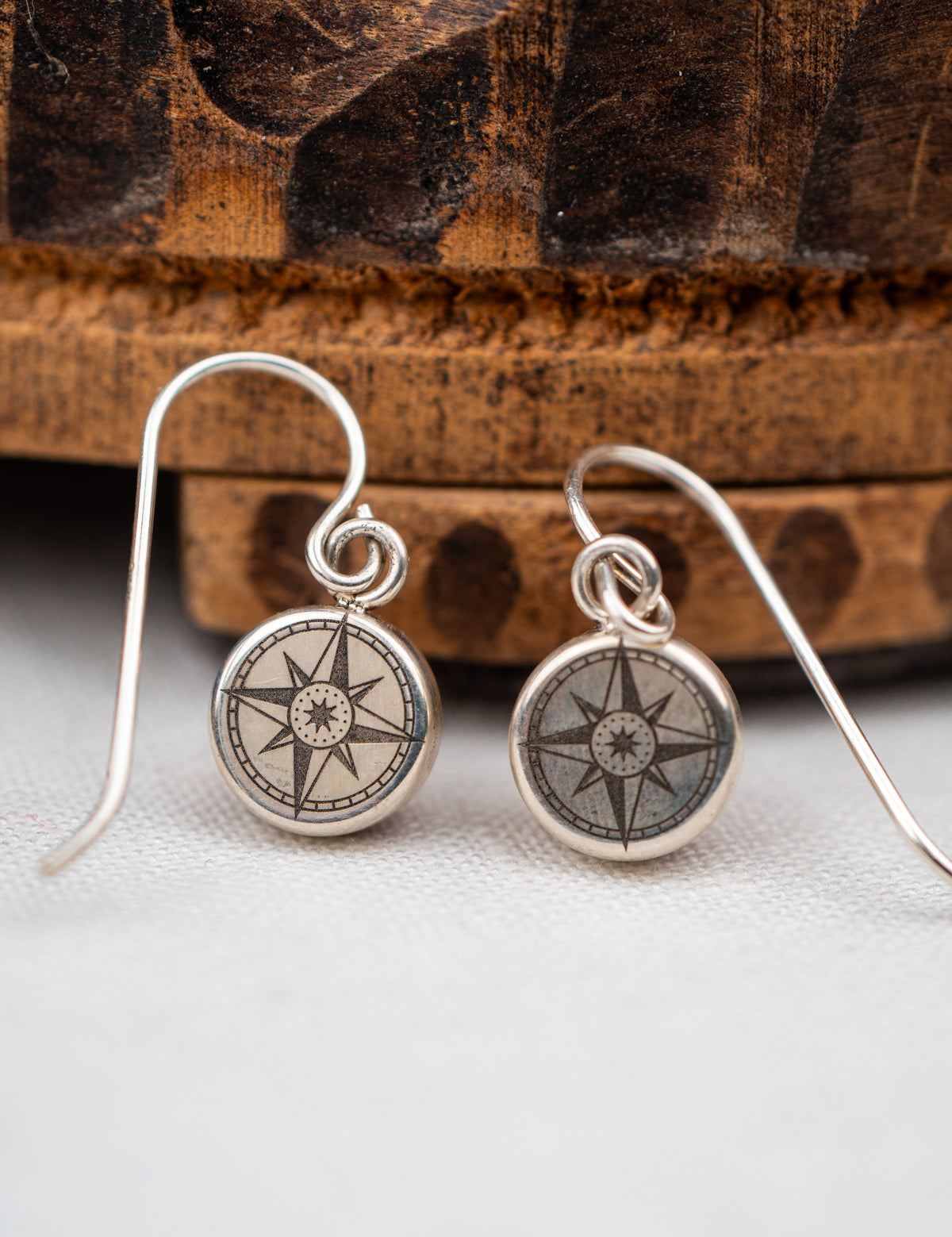 Silver compass-themed earrings on a wooden surface
