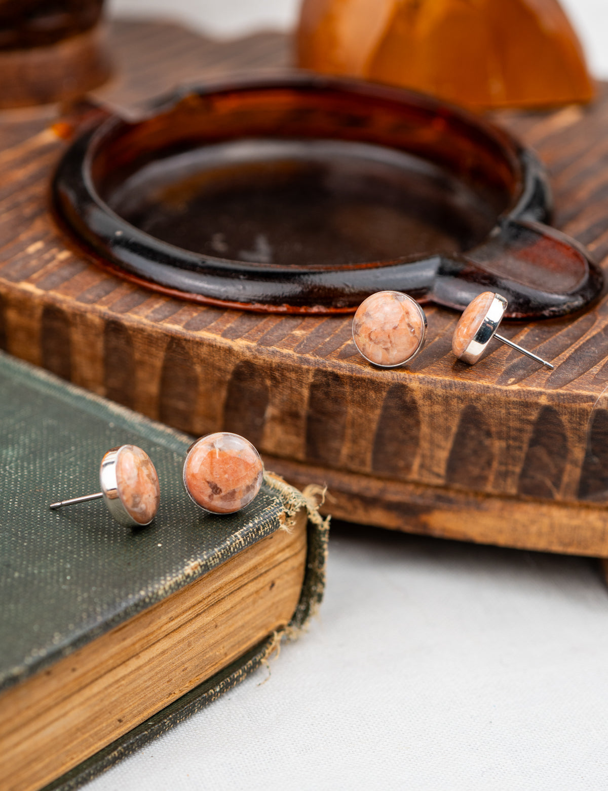 Pair of peach-colored earrings on a wooden surface with a book underneath