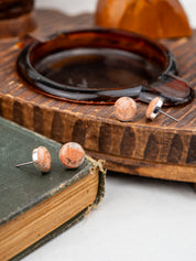 Pair of peach-colored earrings on a wooden surface with a book underneath