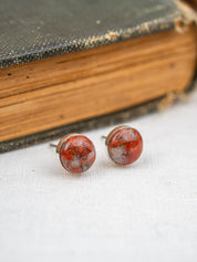 Pair of red and brown speckled granite earrings on a white surface with an old book in the background.