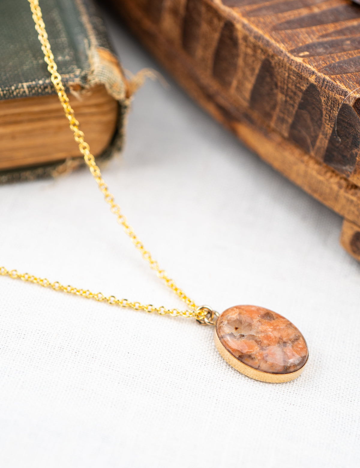 Gold necklace with an oval pendant on a white surface with an old book in the background