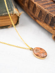 Gold necklace with an oval pendant on a white surface with an old book in the background