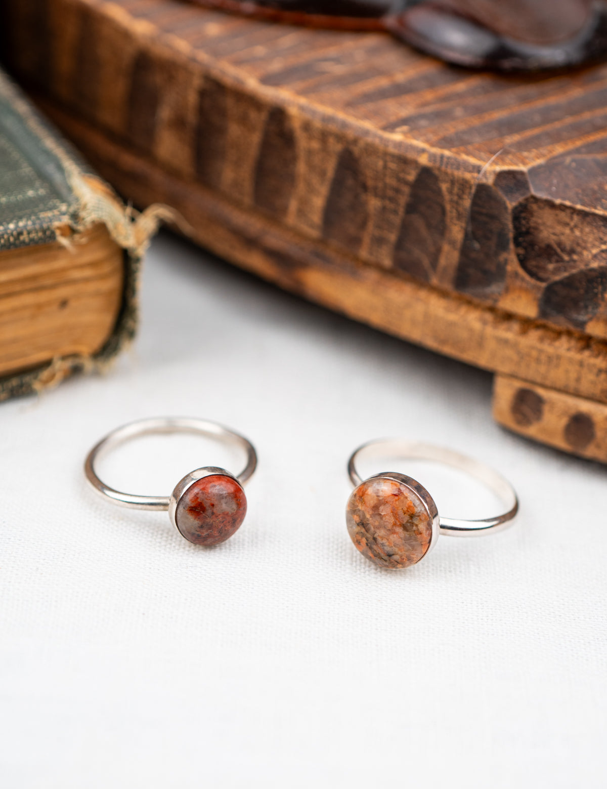 Two silver rings with red stone inlays on a white surface with an old book in the background.