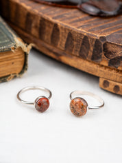 Two silver rings with red stone inlays on a white surface with an old book in the background.