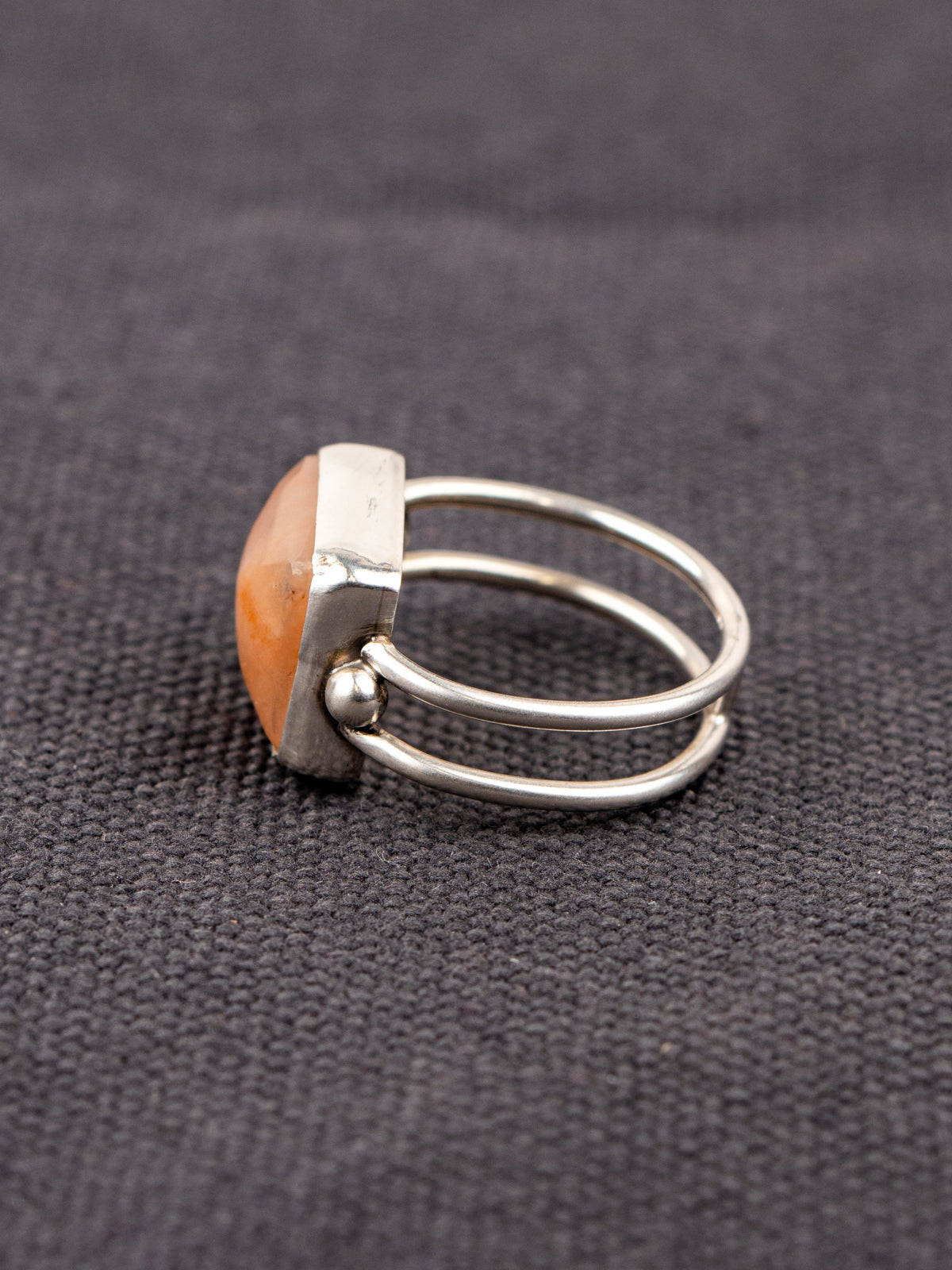 Side profile of a silver ring with a double band design featuring a soft pink opal stone, displayed on a dark fabric background.