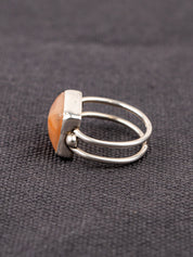 Side profile of a silver ring with a double band design featuring a soft pink opal stone, displayed on a dark fabric background.