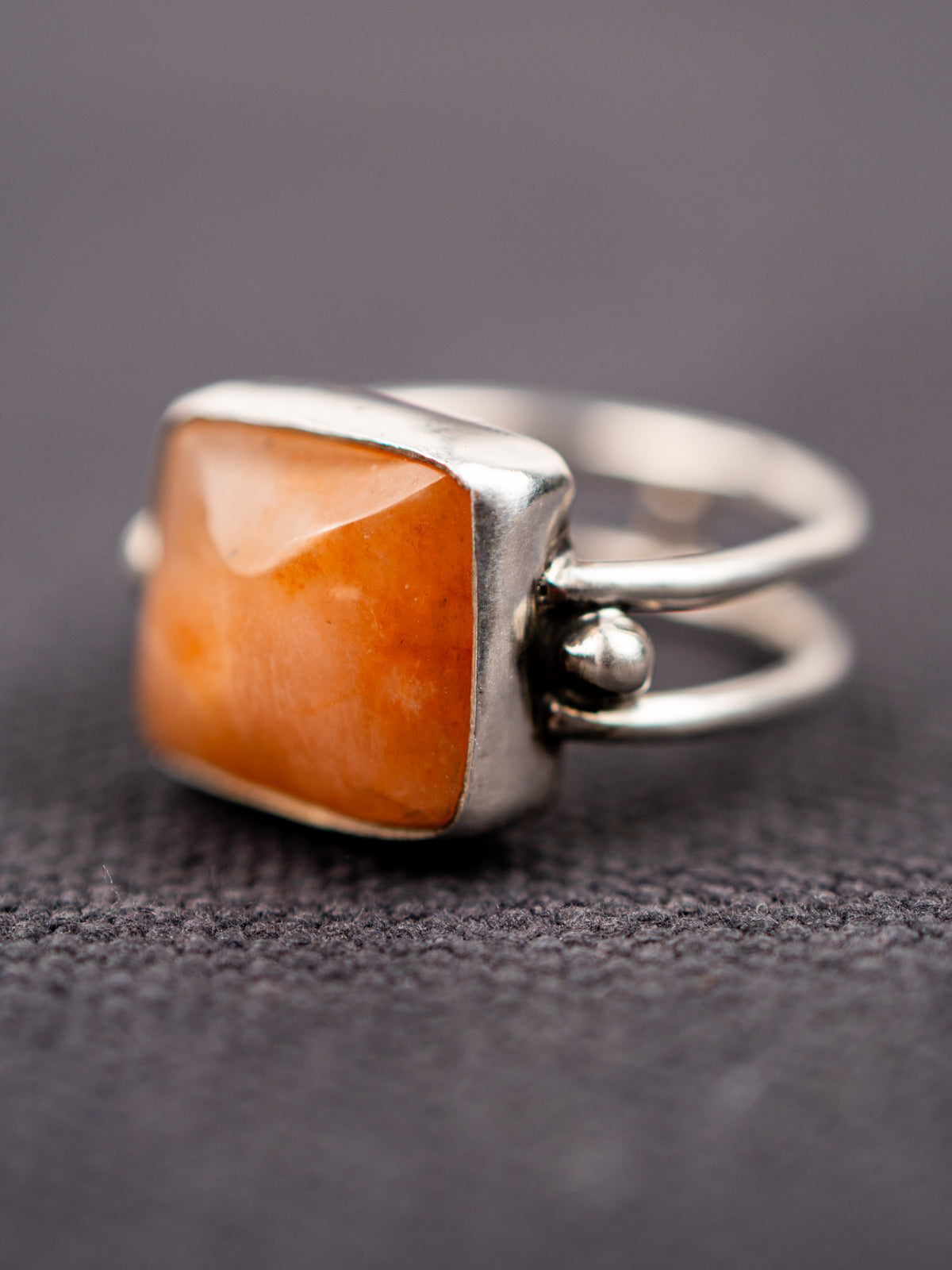 Close-up of a silver ring with a double band design featuring a soft pink opal stone, displayed on a dark fabric background.