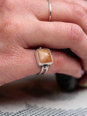 Silver ring with a double band design featuring a soft pink opal stone, displayed on the pinkie finger.