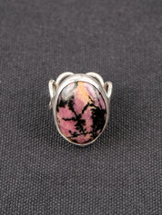Silver ring with a loop band design featuring a pink and black Rhodonite stone, displayed on a dark fabric background.