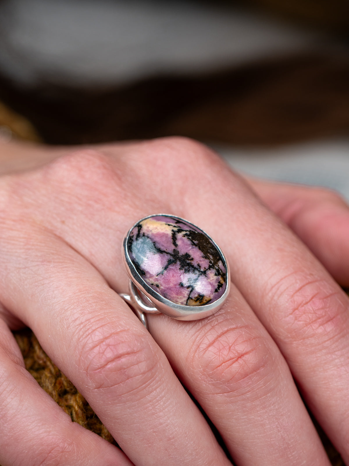 Silver ring with a loop band design featuring a pink and black Rhodonite stone, displayed on hands.