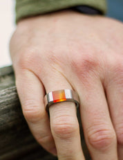 Close-up of a hand wearing a stainless steel signet ring made from a colorful orange stone