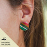 Close-up of a colorful round earring worn by a person with the text "you send the stone" in the corner